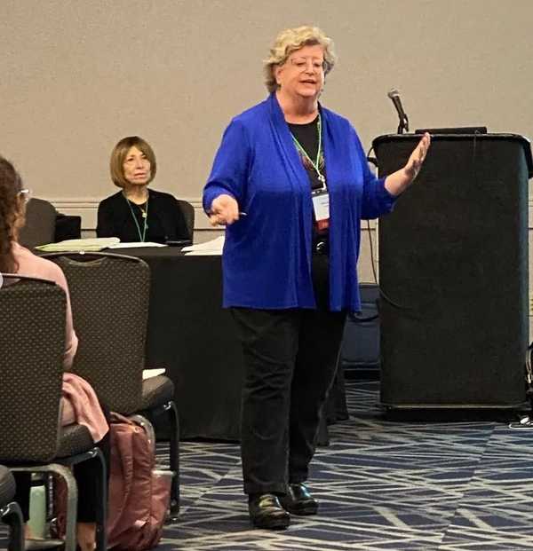 Sheila Fesko (standing) talks to attendees while Karen Flippo (seated, in black) listens.