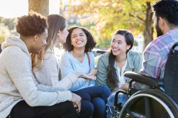 A group of racially and ethnically diverse youth, some with disabilities, are sitting together, talking and laughing.
